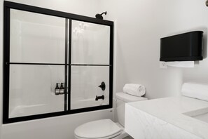 A bathroom with a glass-enclosed shower, a white toilet, and a marble sink.