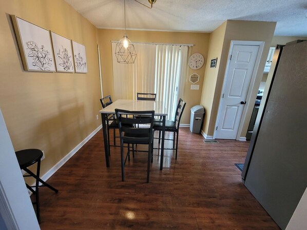 A dining area with a table and chairs, a hanging light fixture, a clock, and a door leading to another room.