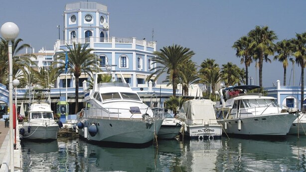 A marina with several yachts docked, a large building with a tower, and palm trees in the background. - Lovely! Close to marina, beaches and town (Estepona)