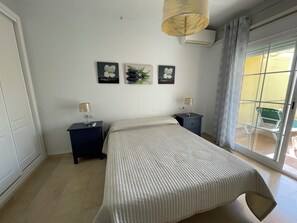 Un dormitorio con una cama, dos mesitas de noche, una lámpara colgante y tres cuadros en la pared.