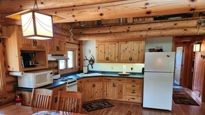 Ein Holzblockhaus im Inneren mit einer Küche, die Holzschränke, einen Herd, eine Mikrowelle und einen Kühlschrank beinhaltet.