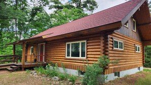 Eine Blockhütte mit Veranda, großen Fenstern und einem roten Dach.