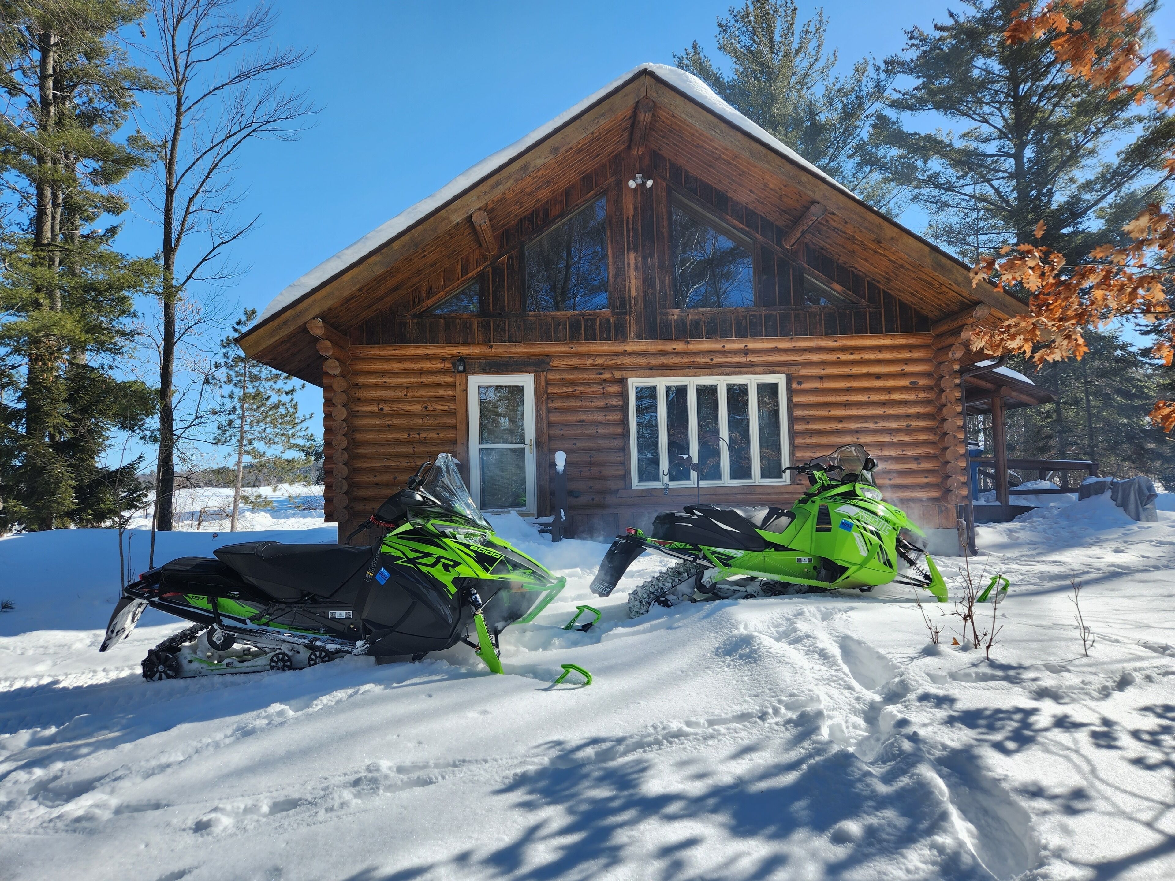 A log cabin with two snowmobiles parked in front.