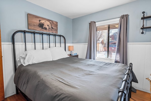Un dormitorio con cama, una ventana con cortinas, una mesita de noche y una repisa en la pared.