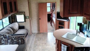 An RV interior with a kitchenette, a seating area, and a door leading to a bedroom.