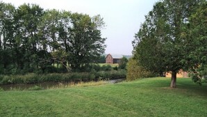 A grassy field with a small stream, trees, and a distant barn.