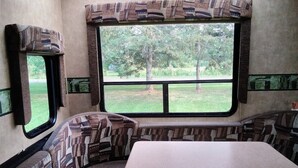 A compact RV interior with a large window, patterned upholstery, and a central table.