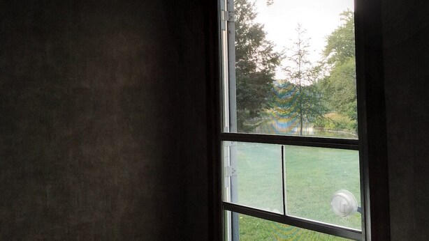 A bedroom with a large window, a bed, and a view of a grassy area.