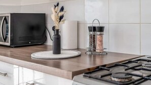 A kitchen with a microwave, a vase with dried flowers, a salt and pepper shaker, and a gas stove. - 3-Bed House Near Lakeside Mall | Free Parking




















 (Essex)