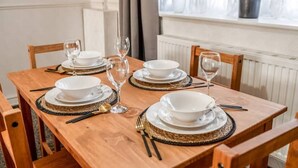 A dining table set with white plates, bowls, and cutlery, surrounded by wooden chairs. - 3-Bed House Near Lakeside Mall | Free Parking




















 (Essex)