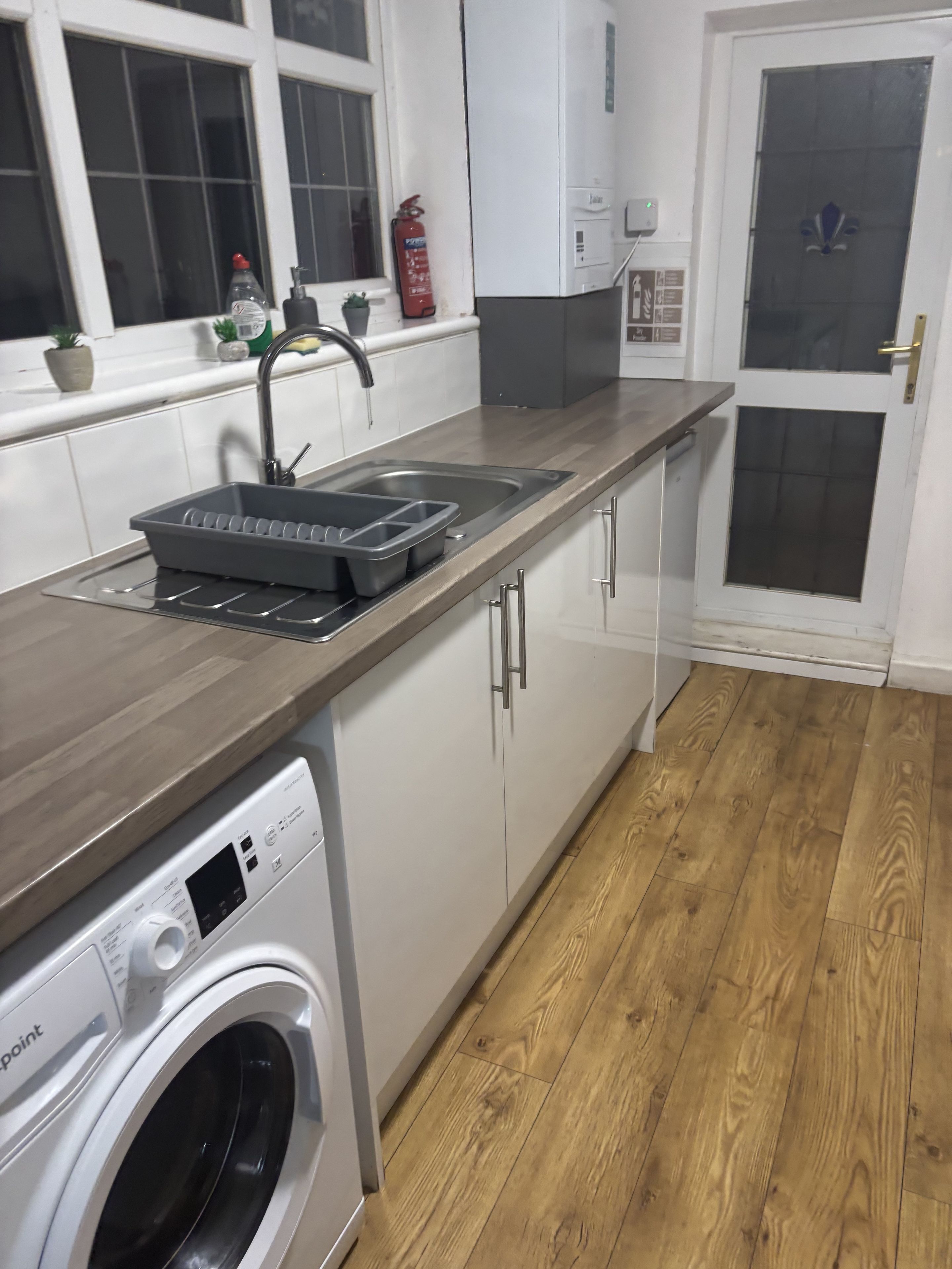 A modern kitchen with a built-in washing machine, a stainless steel sink, and a fire extinguisher.