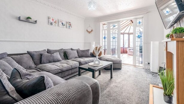 A modern living room with a sectional sofa, a coffee table, and a flat-screen TV mounted on the wall. - 3-Bed House Near Lakeside Mall | Free Parking




















 (Essex)