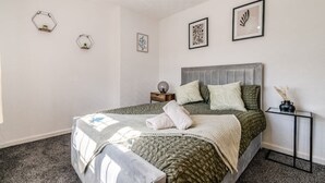 A bedroom with a bed, a nightstand, a wall-mounted shelf, and three wall art pieces. - 3-Bed House Near Lakeside Mall | Free Parking




















 (Essex)