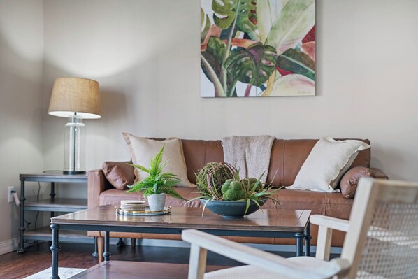 A living room with a brown leather sofa, a coffee table with a plant, a lamp, and a painting on the wall.