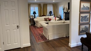 Un salon avec un canapé beige, un tapis à motifs rouges et noirs et un parquet foncé.