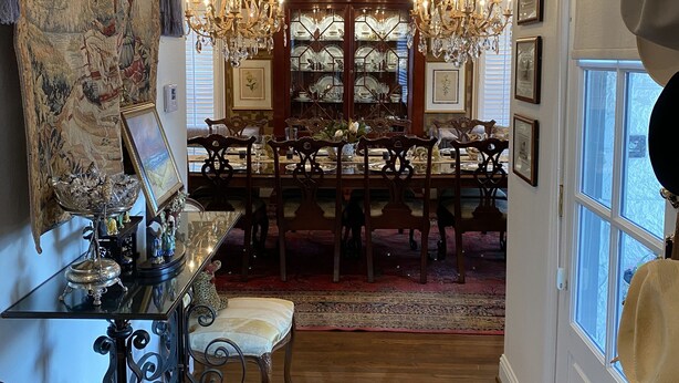 Une salle à manger avec un lustre, une table à manger en bois, des chaises et un grand tapis.