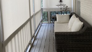 Un balcon avec un canapé en osier et une petite table, des murs blancs et un plancher en bois.