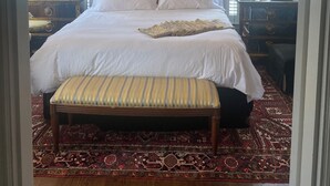 Une chambre spacieuse avec un grand lit, un lustre, un banc et un tapis à motifs.