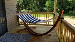 A hammock chair on a wooden deck with a view of a grassy area and trees. - Cozy tiny home w/lofts deck grill hammock (Phenix City)