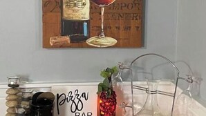 Een houten wand met een schilderij van een wijnfles en glas, een bord met een pizzeria en een glazen karaf op een houten tafel.