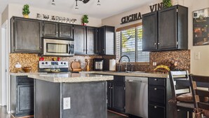 Cozinha com armários escuros, uma ilha central, eletrodomésticos de aço inoxidável e backsplash com mosaicos.