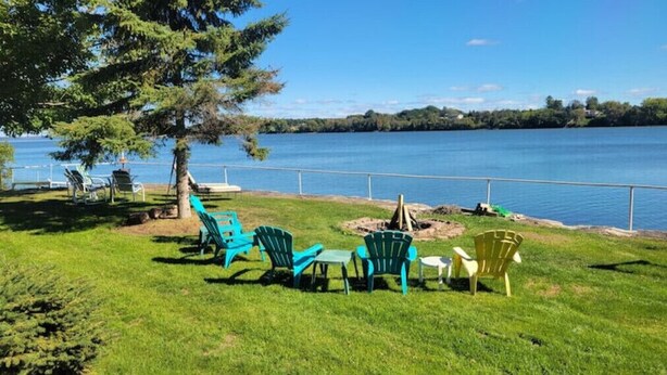 A lakeside seating area with chairs and tables, a tree, and a view of the lake. - Cottage on Hay Bay. Private boat launch & dock.
 (Greater Napanee)