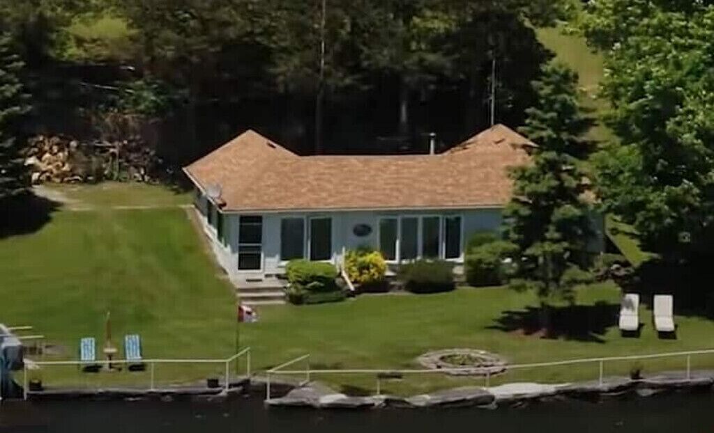 Une maison avec un toit en pente, une pelouse bien entretenue et une jetée qui s’avance sur une étendue d’eau.