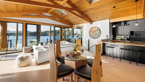 A modern kitchen with a large island, wooden ceiling beams, and a view of the lake. - Kingfisher Manor (Sooke)