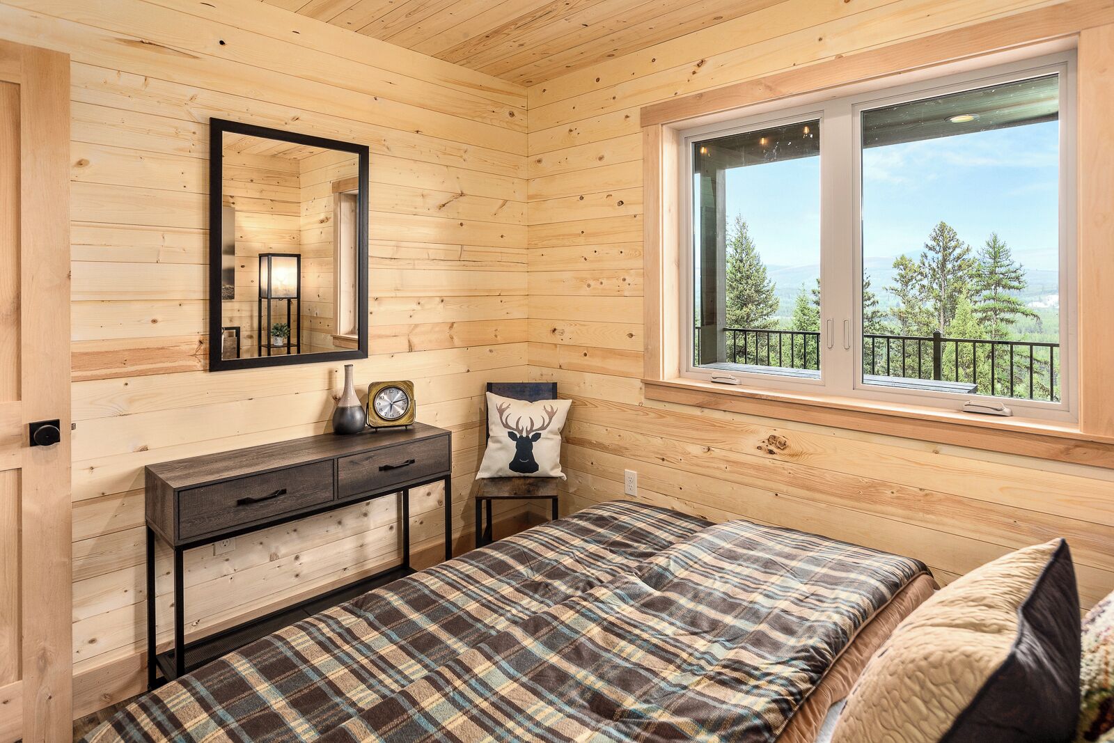 A wooden cabin room with a bed, a dresser, a mirror, and a window with a view of trees.