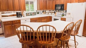 A kitchen with wooden cabinets, a white countertop, a central island with chairs, a microwave, a refrigerator, and a window with a view of greenery. - 669 Rainbow Landing Dr (Cotter)