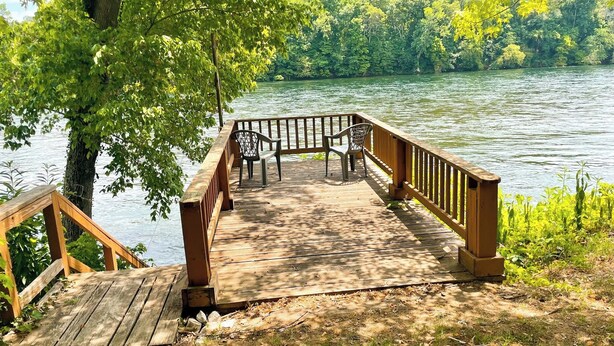 A wooden deck with a railing, benches, and a view of a lake surrounded by trees. - 669 Rainbow Landing Dr (Cotter)