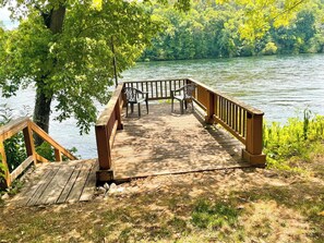 A wooden deck with a railing, benches, and a view of a lake surrounded by trees.