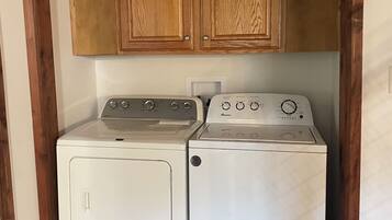 A laundry room with two white front-loading washers and dryers, wooden cabinets above, and a patterned rug on the floor.