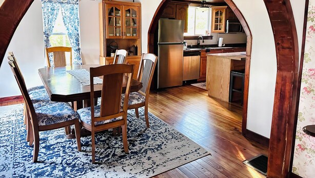 Een eethoek met een tafel en stoelen, houten kasten, en een keuken met een boogvormige doorgang.