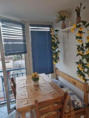 Et spiseområde med et træbord og stole, en vase med blomster, samt udsigt til det udendørs gennem store vinduer.