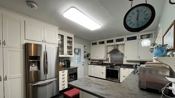 Una cocina moderna con electrodomésticos de acero inoxidable, armarios blancos y un reloj grande.