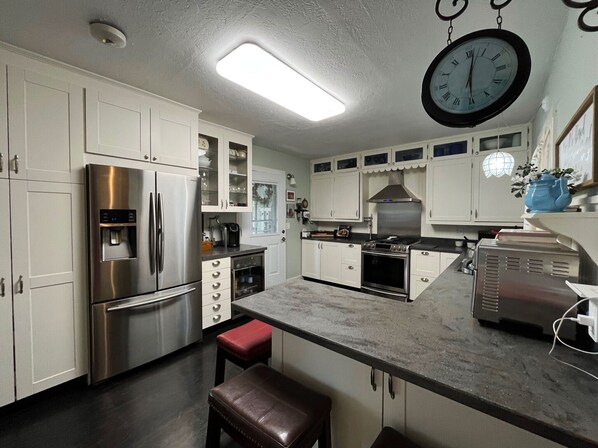 A modern kitchen with stainless steel appliances, white cabinetry, and a large clock. - Greenstone Cottage (Oconomowoc)
