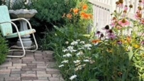 Un jardín con un sendero de piedra, una silla verde y diversas plantas florecientes.
