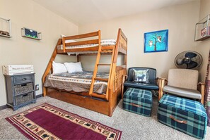 A bunk bed with a wooden frame, a small bedside table, a chair, a fan, and a rug. - Ponderosa Hill Cabin (Big Bear City)