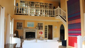 Ein geräumiges Wohnzimmer mit Kamin, einem weißen Sofa, einem Bücherregal und einer Treppe, die zu einer oberen Ebene führt.