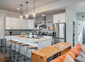 Cocina moderna con armarios blancos, un refrigerador de acero inoxidable, una isla central con taburetes e iluminación colgante.
