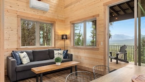 Ein gemütliches Blockhaus-Interieur mit einer Couch, Tisch und Stühlen, große Fenster mit Blick auf Bäume und Berge.