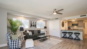 A modern living room with a sofa, armchair, coffee table, and a dining area with stools. - Gated community, private beach access, renovated condo!! (Ponte Vedra Beach)