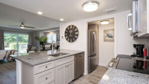 A modern kitchen with a central island, stainless steel appliances, and a large wall clock. - Gated community, private beach access, renovated condo!! (Ponte Vedra Beach)