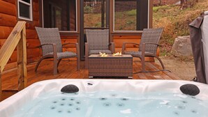Una terraza de madera con un jacuzzi, sillas de mimbre y una chimenea.