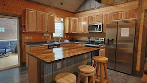 Una cocina con armarios de madera, un refrigerador de acero inoxidable, un microondas y una isla grande con taburetes.