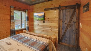 Habitación de cabaña de madera con una cama, un televisor montado y una puerta de madera grande.