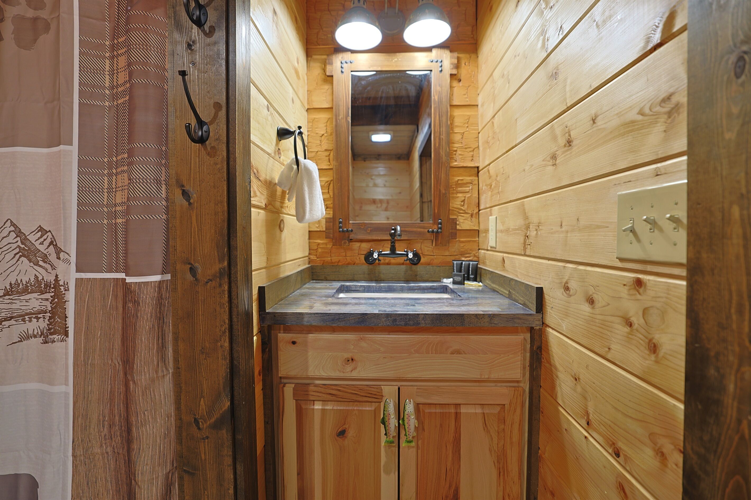 Une salle de bain rustique, aménagée dans une cabane en bois, avec un lavabo, un miroir, un porte-serviettes et des armoires en bois.