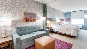 Ein Hotelzimmer mit grauem Sofa, einem Holztisch, einem Bett mit weißer Bettwäsche und einem gerahmten Bild eines Gebäudes an der Wand.