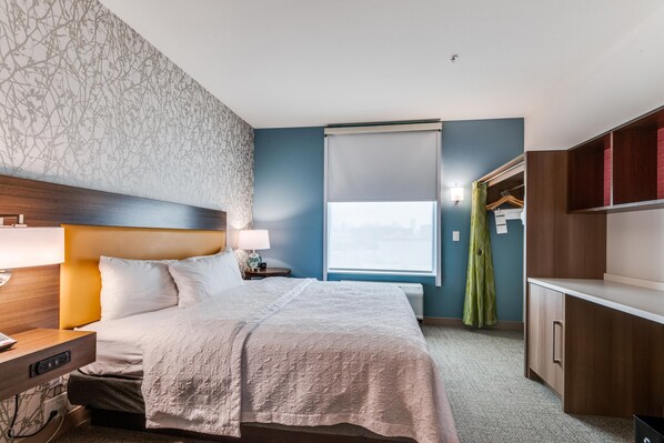 Une chambre d’hôtel comprenant un lit, une table de chevet, une lampe, une fenêtre avec stores et une armoire.